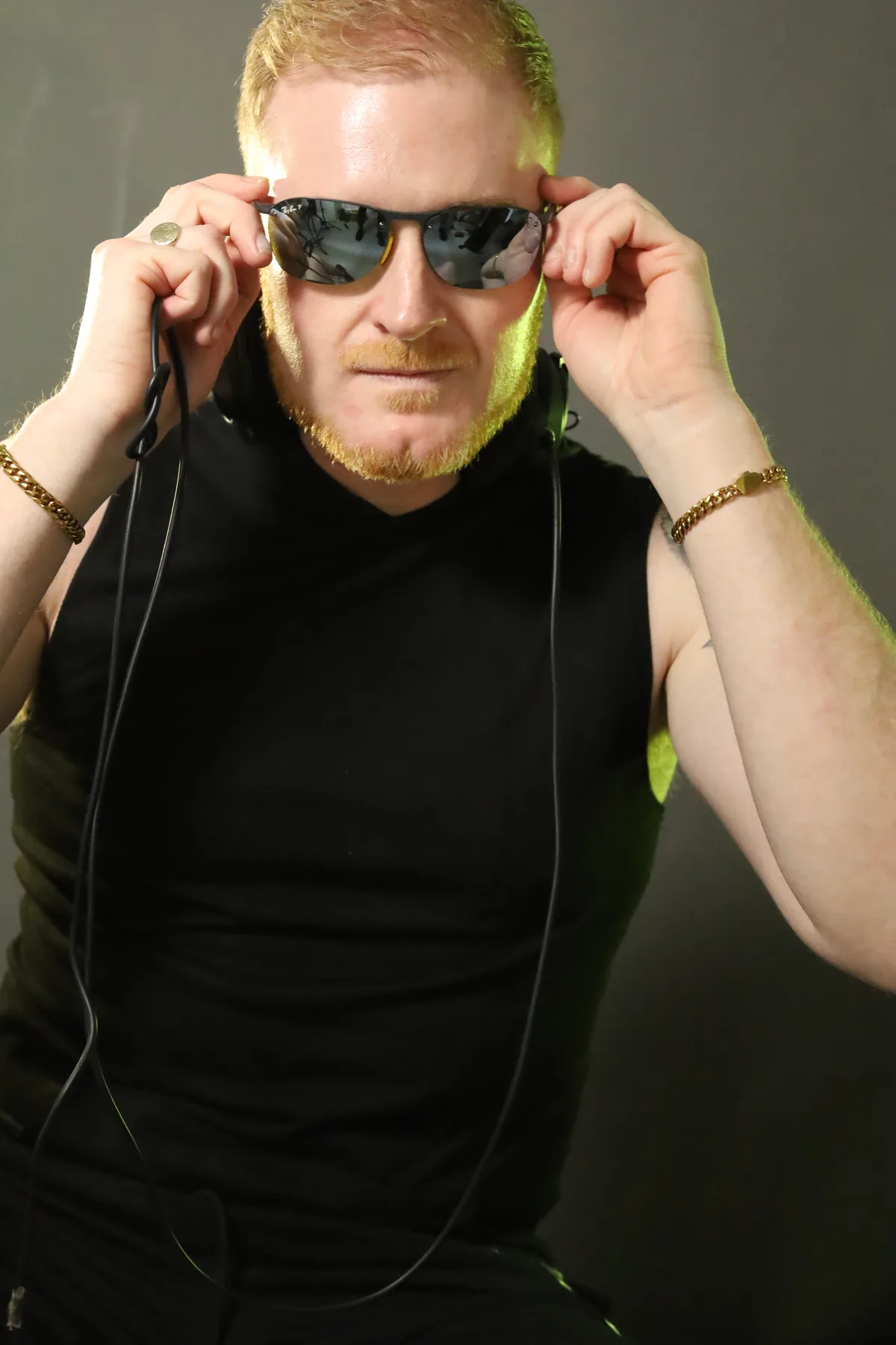 Dave Mladi adjusting his sunglasses with both hands, wearing a black vest