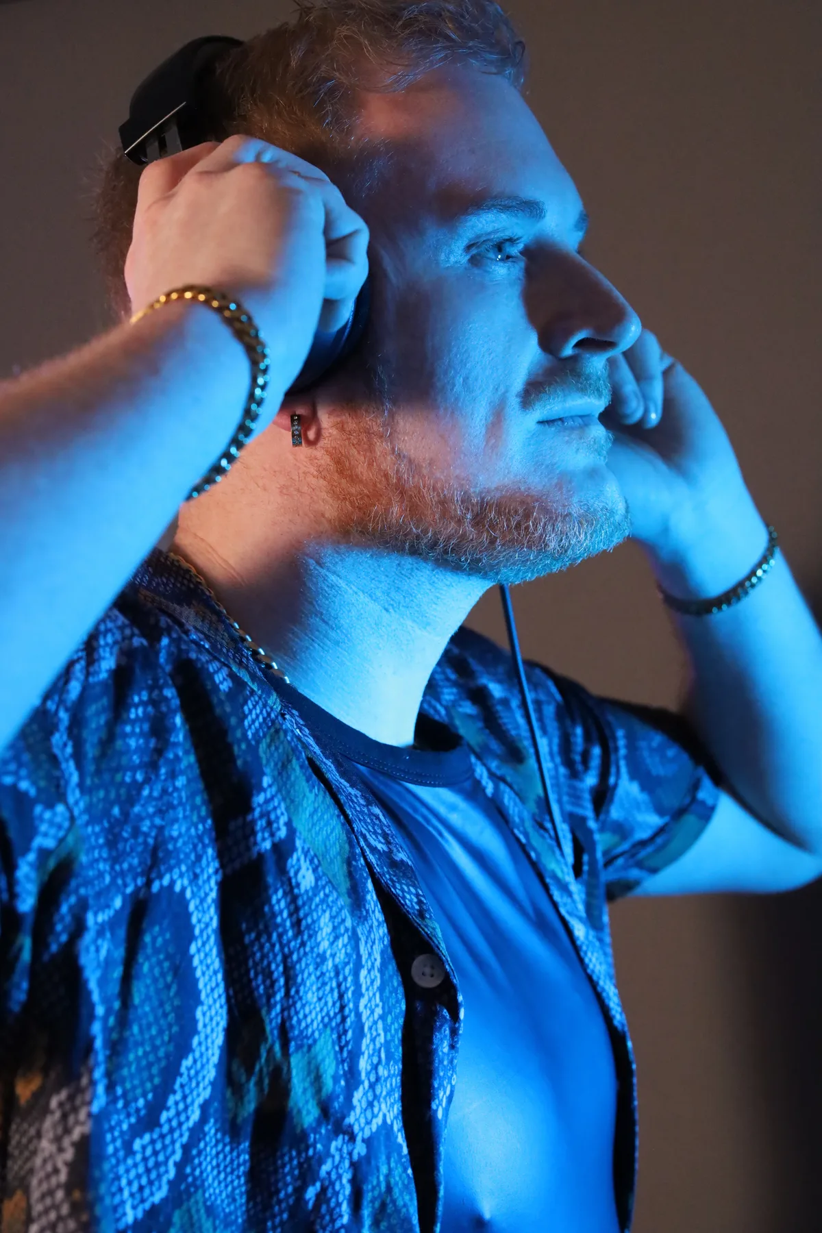Dave Mladi with both hands raised to his head, washed in blue light