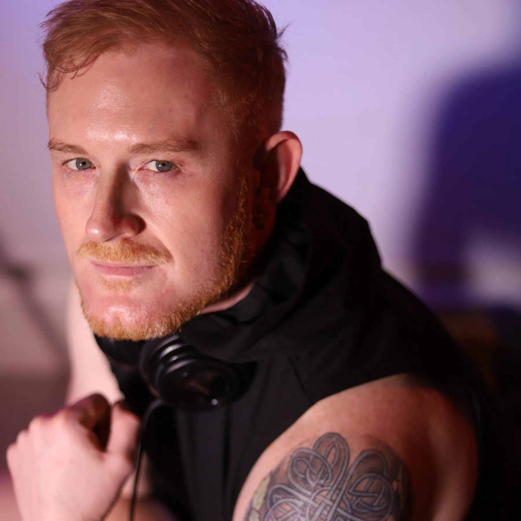 Close-up of Dave Mladi resting his hand on his chin in soft pink studio light