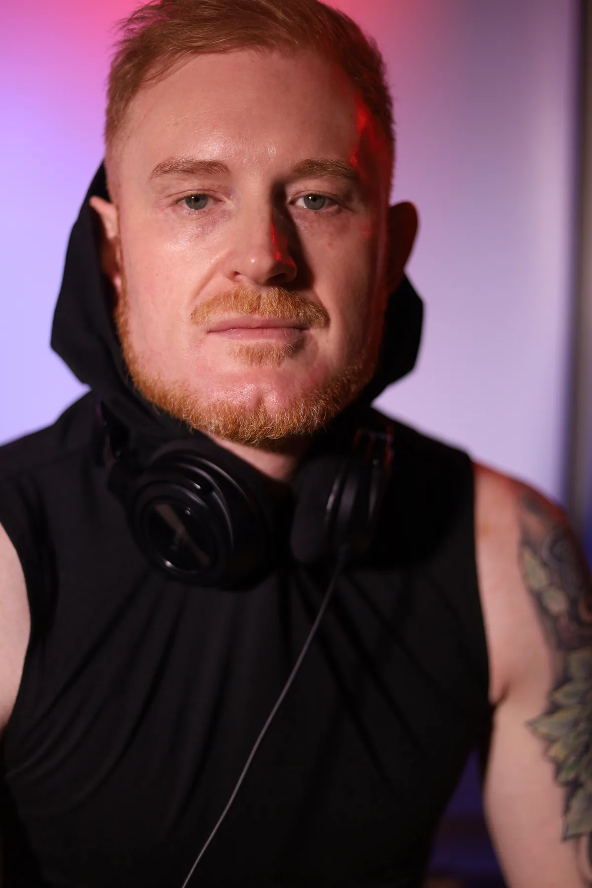 Head and shoulders portrait of Dave Mladi with headphones round his neck in purple light