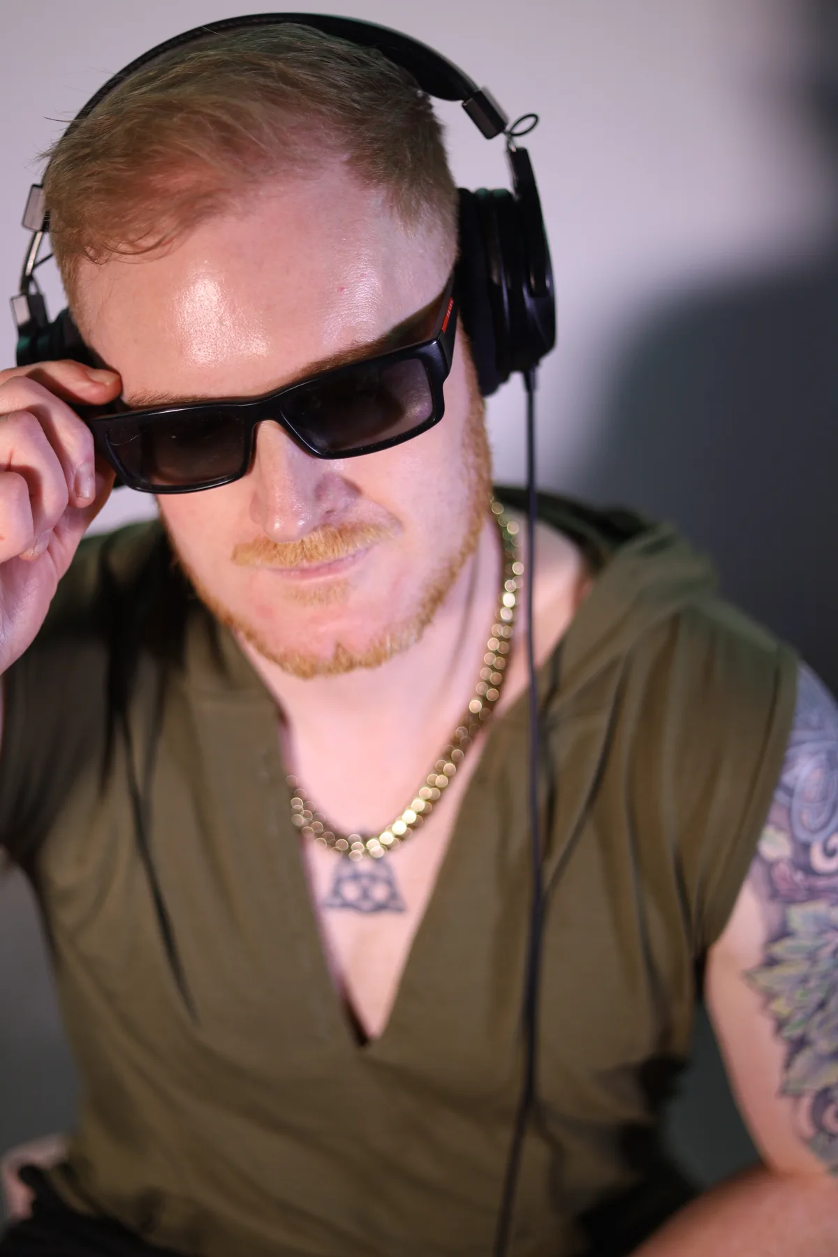Dave Mladi in sunglasses and a khaki vest, one hand on his headphones