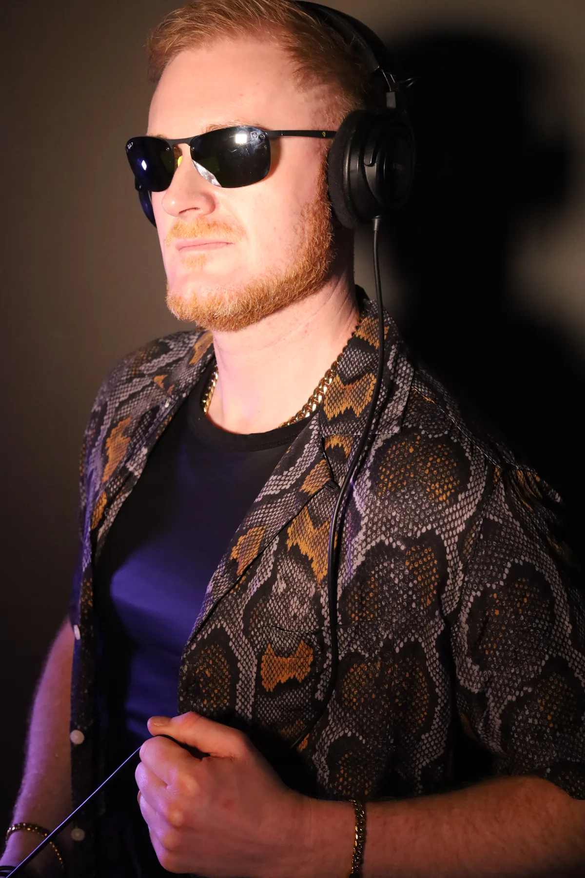Dave Mladi in sunglasses and a patterned shirt in warm amber light
