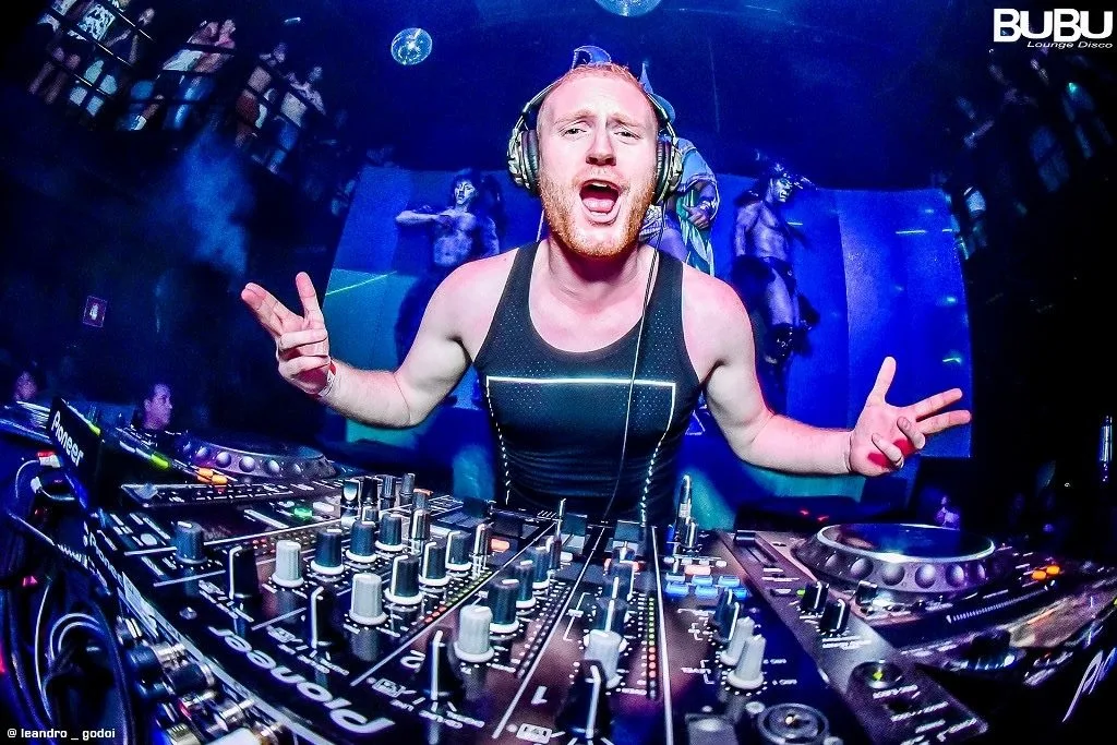 Dave Mladi in headphones, arms wide, playing behind Pioneer decks at BUBU Lounge Disco
